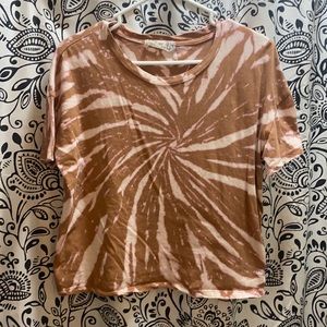 Not sure how I would describe the color but it’s a tan tie dye type shirt!